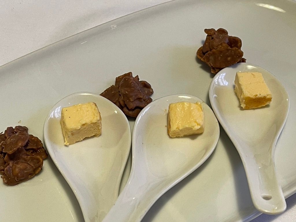 Cuadrados de comida en cucharas y racimos de chocolate en un plato blanco.