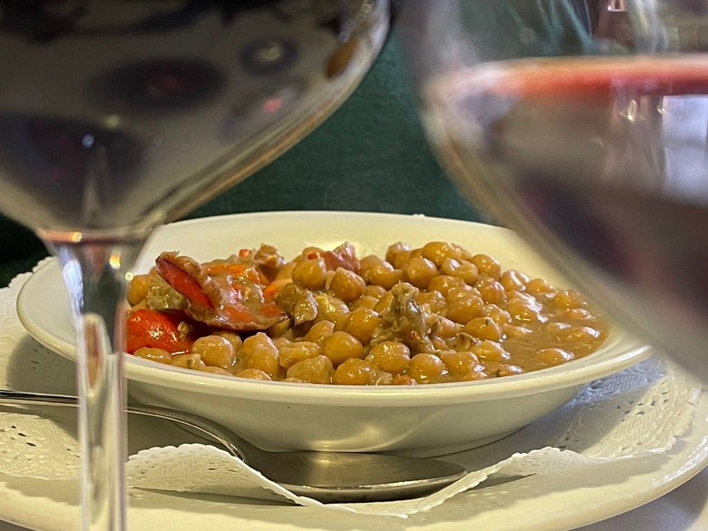 Cuenco de garbanzos con bogavante y tomates, entre dos copas de vino tinto.