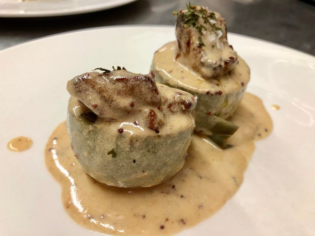 Dos rollitos de verduras verdes cubiertos con champiñones y salsa cremosa en un plato blanco.