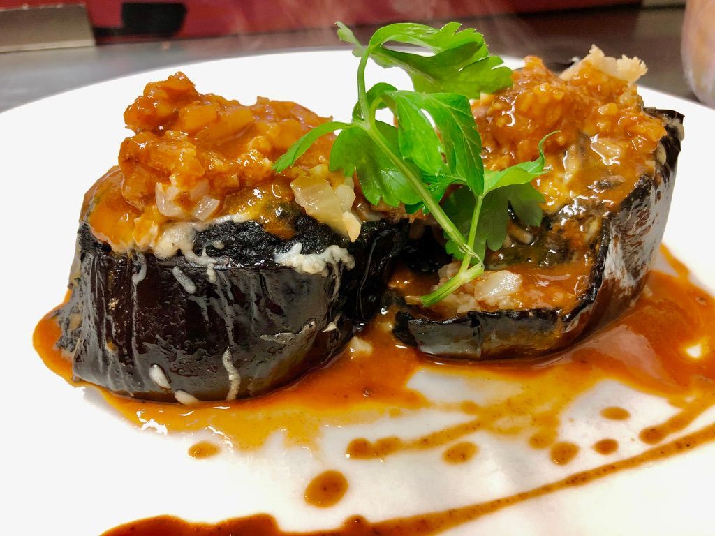 Mitades de berenjena rellenas con salsa de naranja, adornadas con hierbas, en un plato blanco.