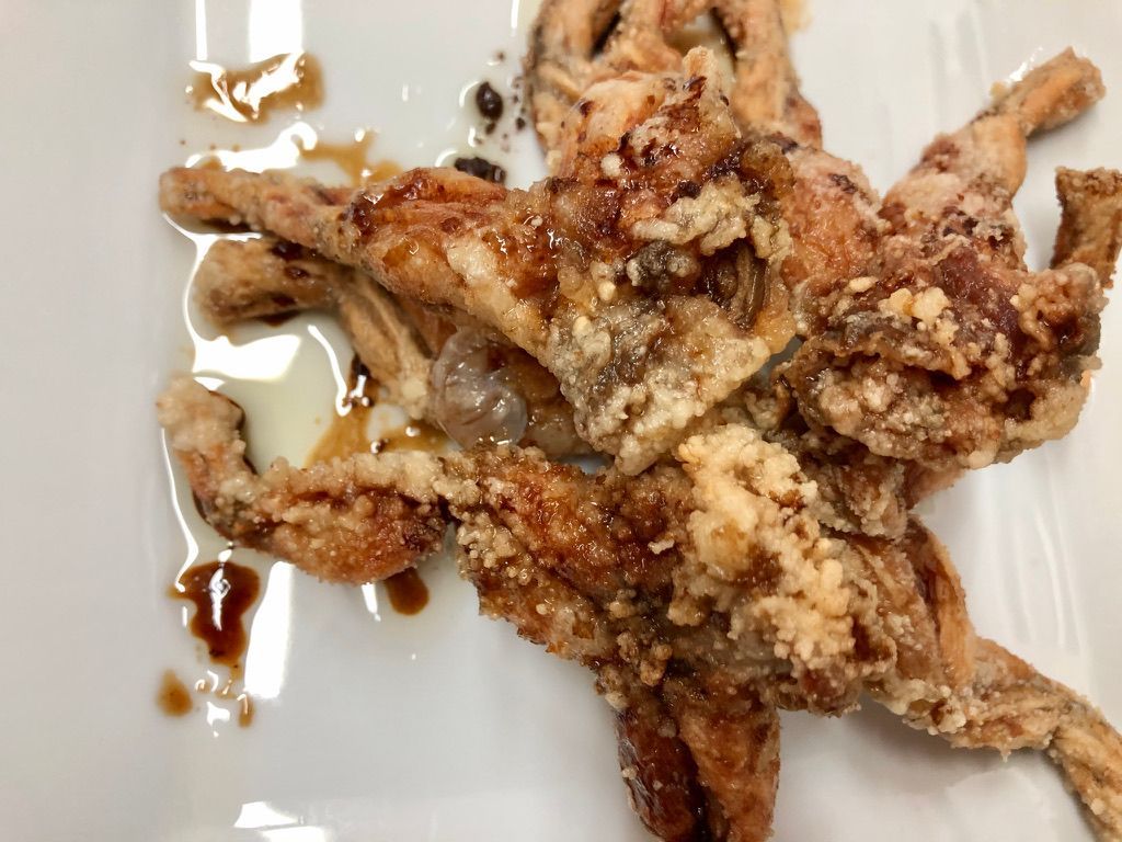 Ancas de rana fritas en un plato blanco, rociadas con salsa.