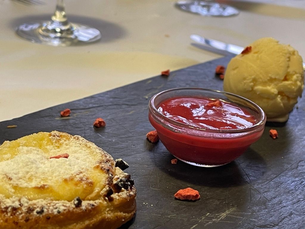 Postre en plato de pizarra: masa de hojaldre, salsa de frambuesa y bola de helado amarillo.