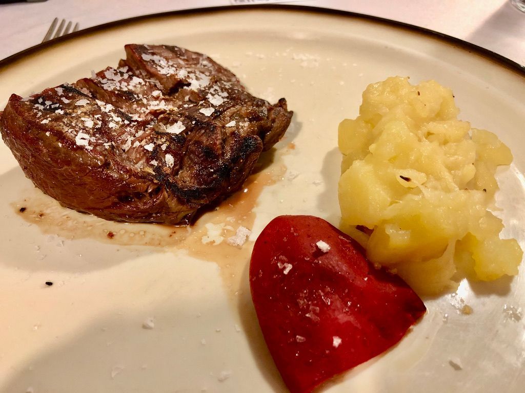 Bistec con polvo blanco, guarnición amarilla y pimiento rojo en un plato blanco.