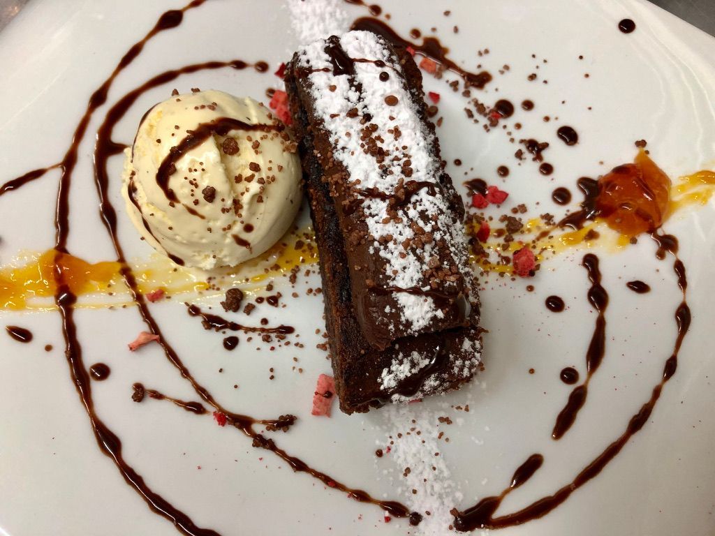 Pastel de chocolate con helado de vainilla en un plato blanco, rociado con salsa de chocolate y adornado.