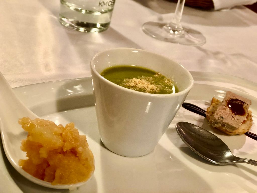 Plato de aperitivo: sopa verde, salsa de naranja en cuchara y hojaldre con aderezo.
