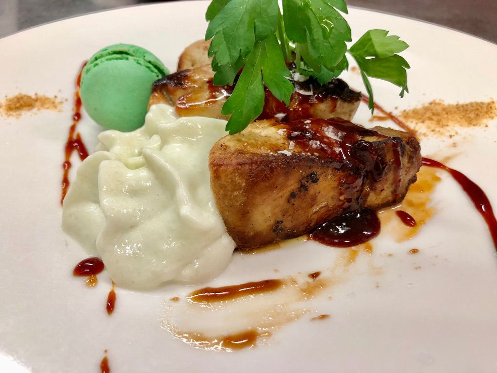 Foie gras salteado con crema batida, macarrón verde, perejil y salsa rociada en un plato blanco.