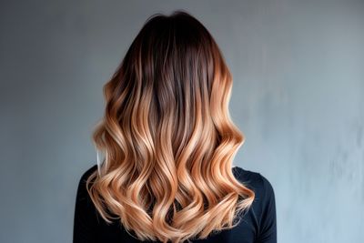 Eine Friseurin mit schwarzen Handschuhen prüft vor schwarzem Hintergrund die Glätte der glatten, braunen Haare ihrer Kundin.