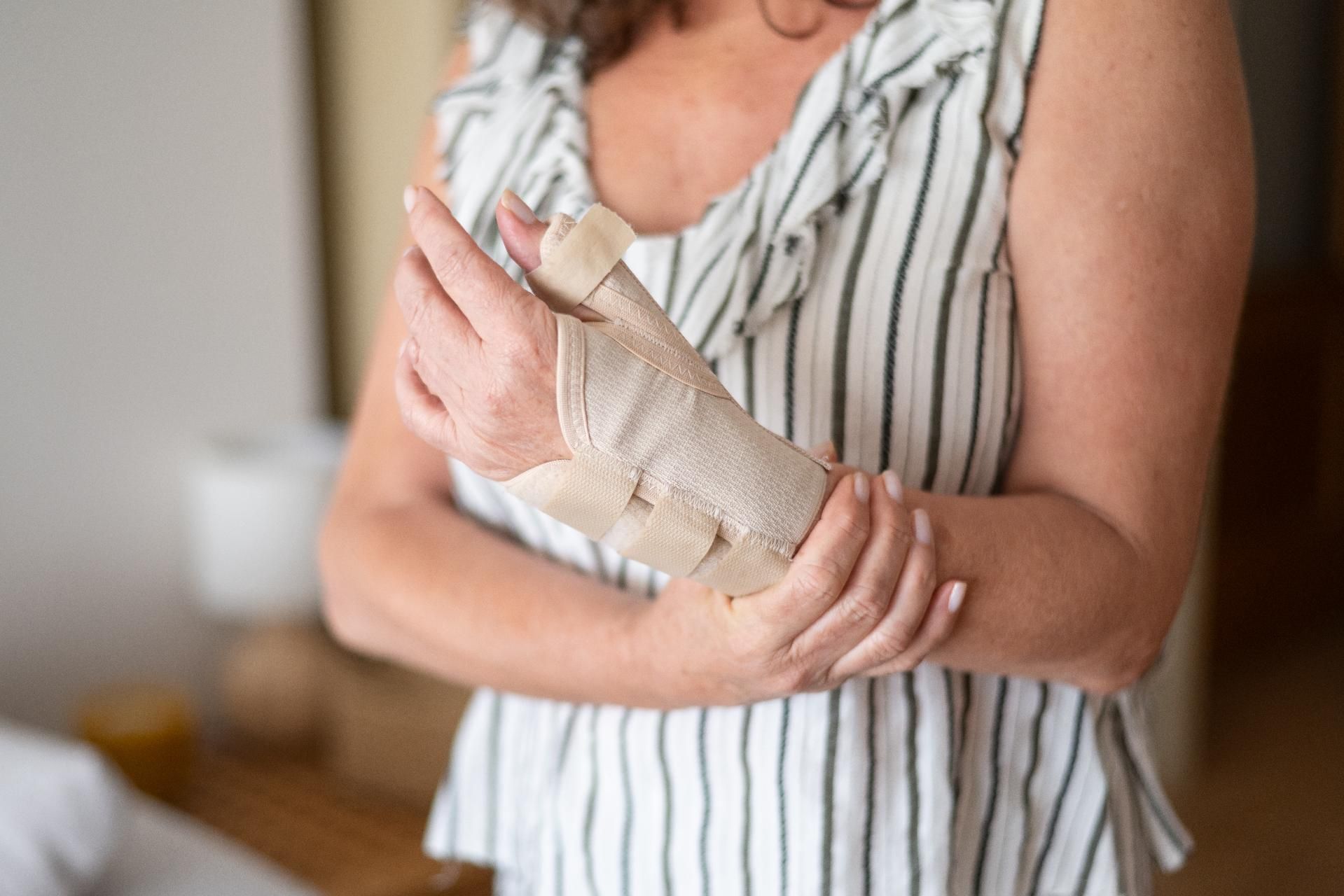 Eine Person mit bandagierter Hand, die ihren Unterarm hält, trägt ein gestreiftes, ärmelloses Oberteil.