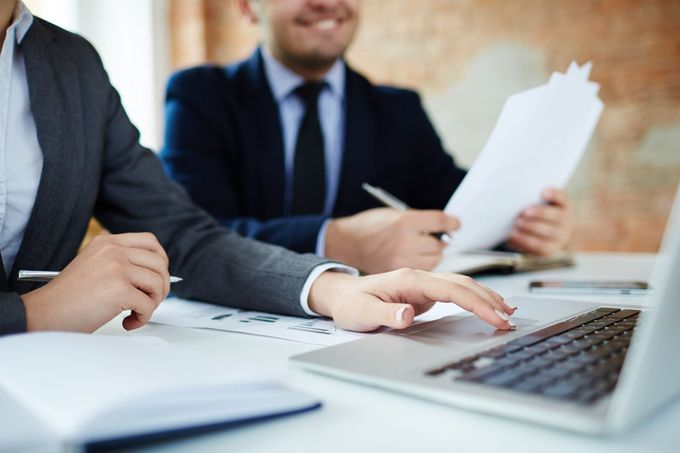 Empresarios con traje revisando documentos y usando un ordenador portátil en una sala de reuniones.