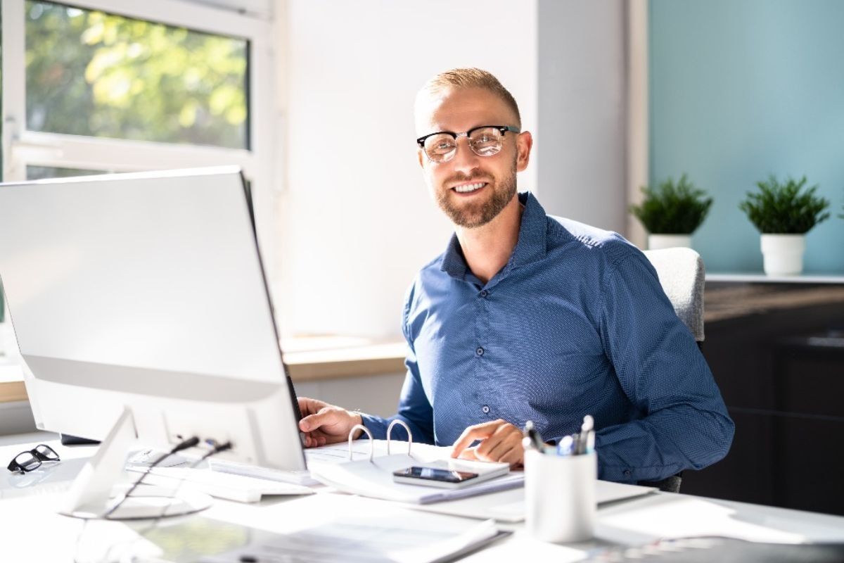 Hombre sonriendo en un escritorio con una computadora en una oficina luminosa.