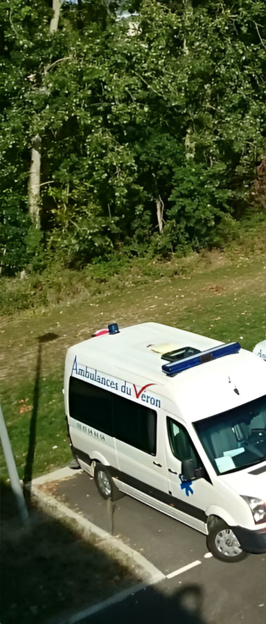 Une ambulance blanche est garée sur un parking goudronné.