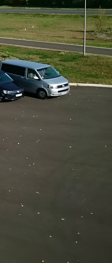Une camionnette argentée et une voiture sombre garées sur l'asphalte, avec de l'herbe verte et une route en arrière-plan.