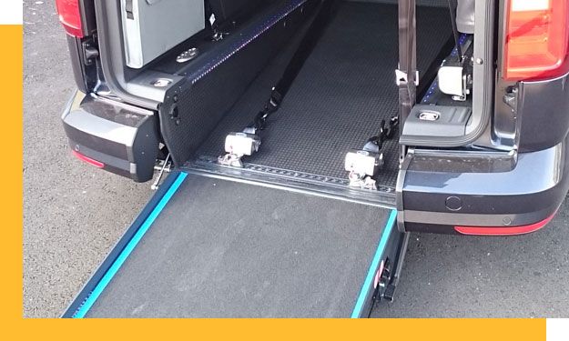 Vue arrière d'une camionnette sombre dont la rampe d'accès pour fauteuil roulant est déployée.