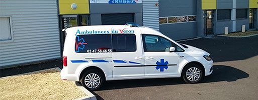 Ambulance blanche ornée du logo de l'étoile de vie bleue, stationnée devant un bâtiment.