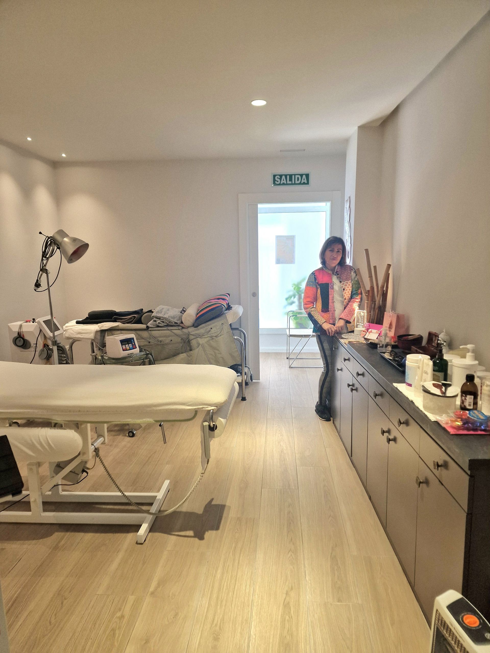 Una mujer está parada en un pasillo junto a una mesa de masajes.