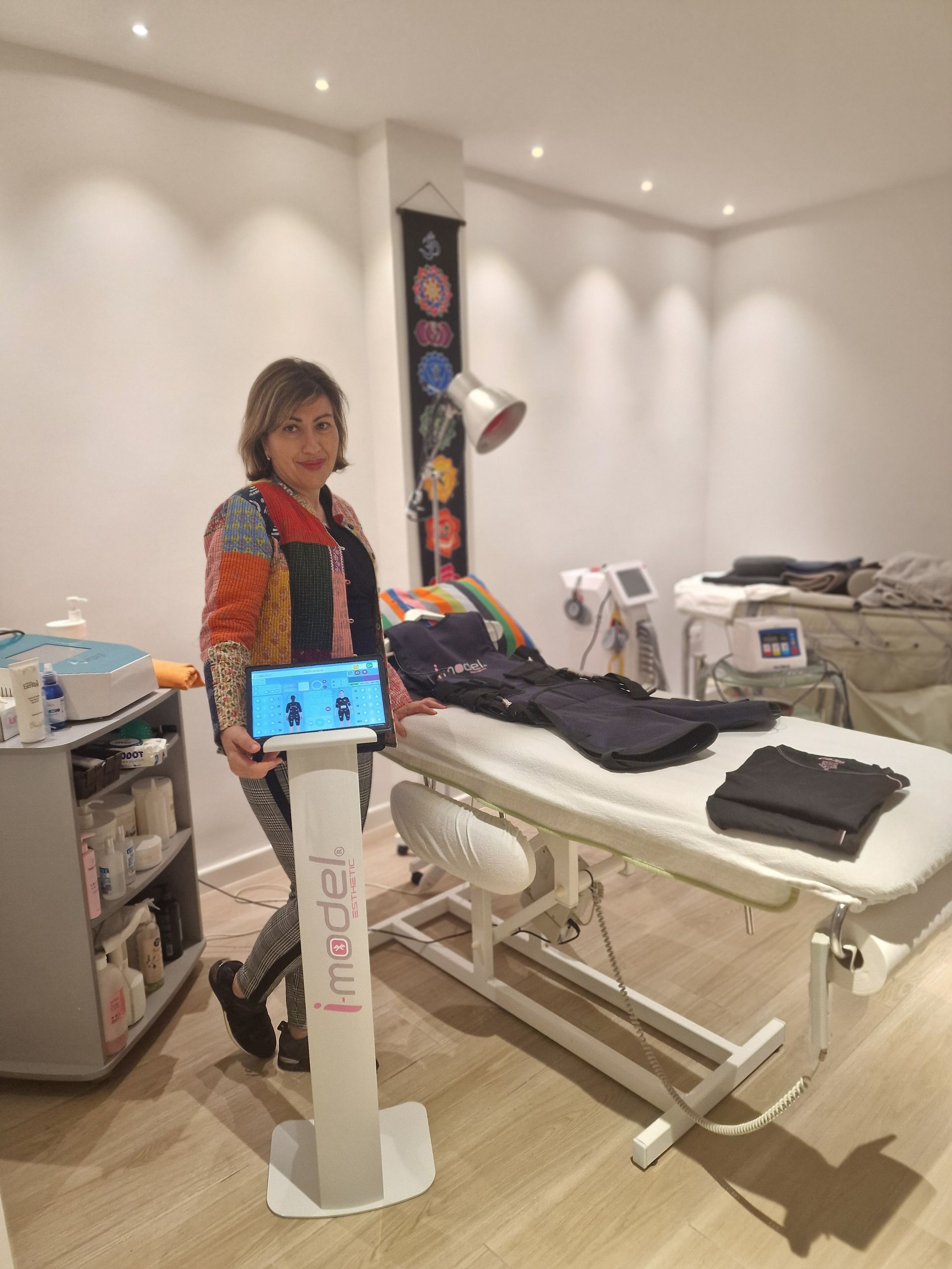 Una mujer está parada frente a una mesa de masajes sosteniendo una tableta.