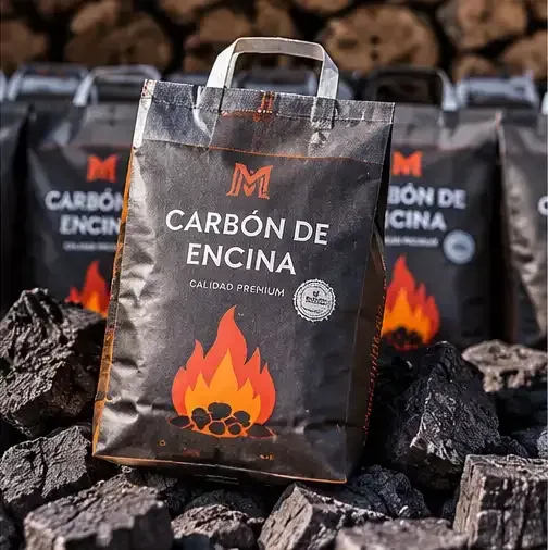 Sacos de carbón etiquetados «Carbón de Encina», con llamas dibujadas, apilados entre trozos de carbón negro.