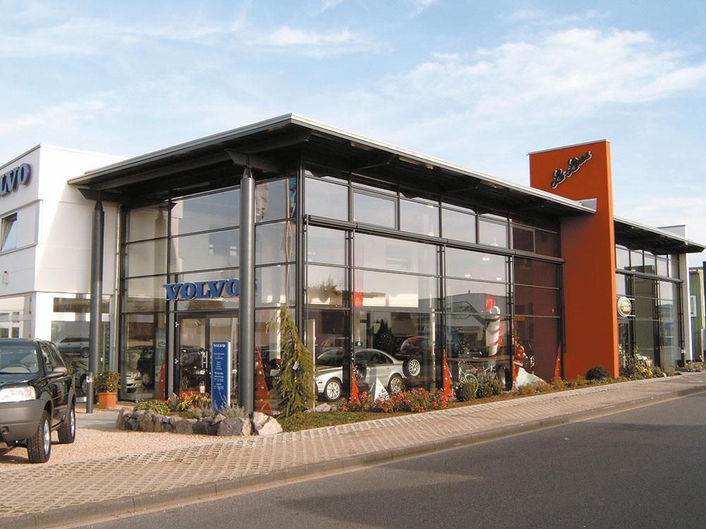 Vor einem Gebäude mit der Aufschrift „Volvo“ steht ein Auto