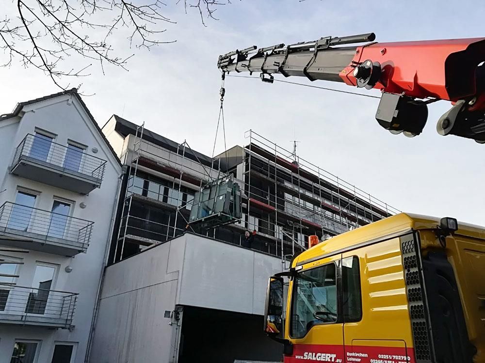 Ein gelber LKW mit einem roten Kran steht vor einem im Bau befindlichen Gebäude.