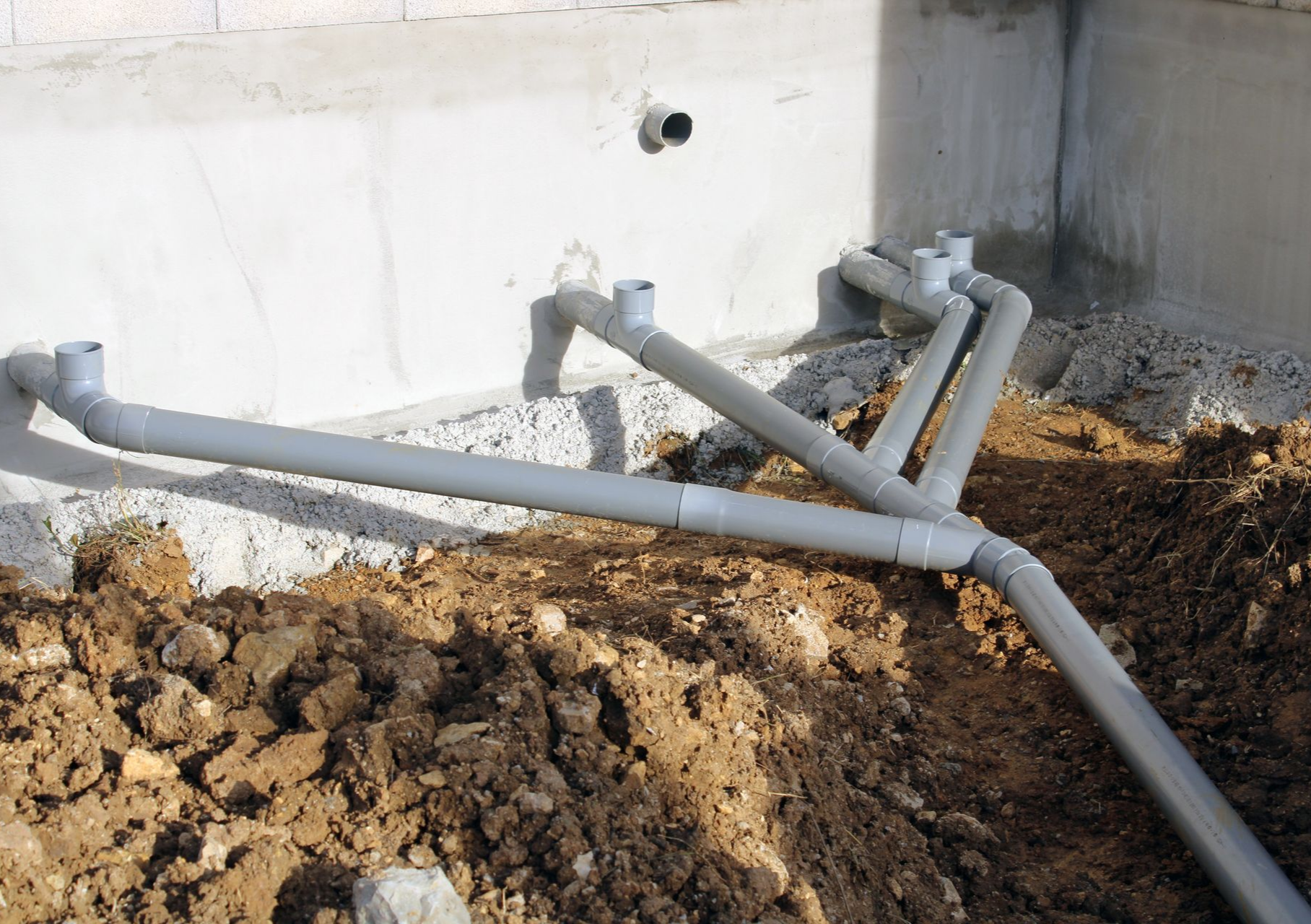 Des tuyaux en PVC gris ont été installés près d'une fondation en béton.