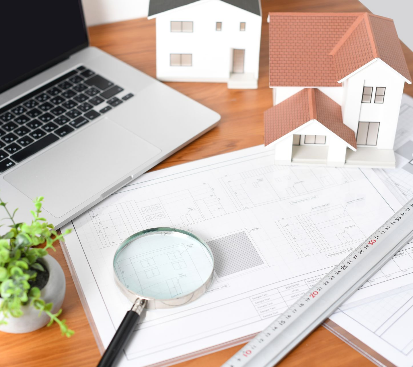 Ordinateur portable, plans architecturaux, loupe, maquettes de maisons sur un bureau.