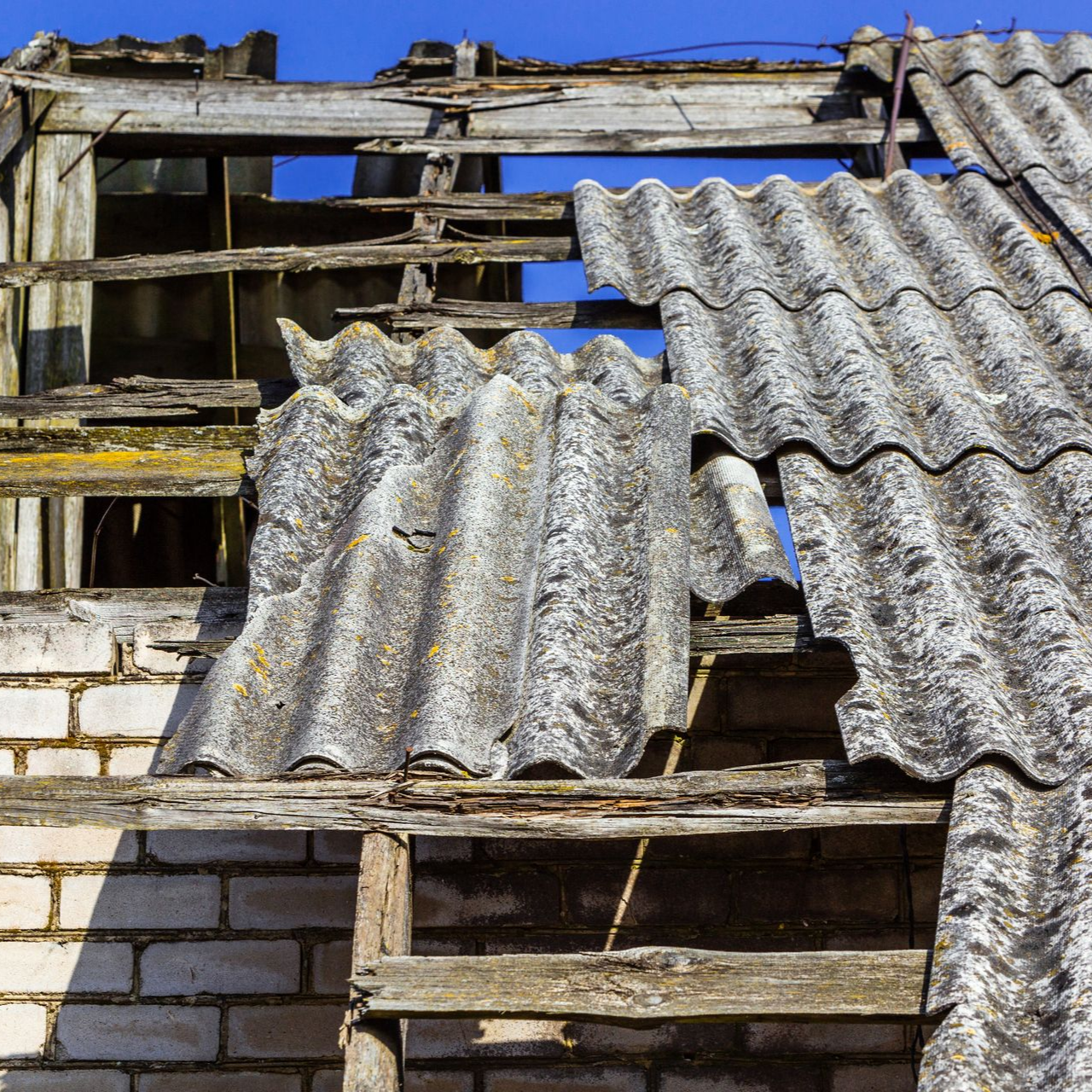 Toiture endommagée avec des panneaux de tôle ondulée manquants sur un bâtiment en briques.