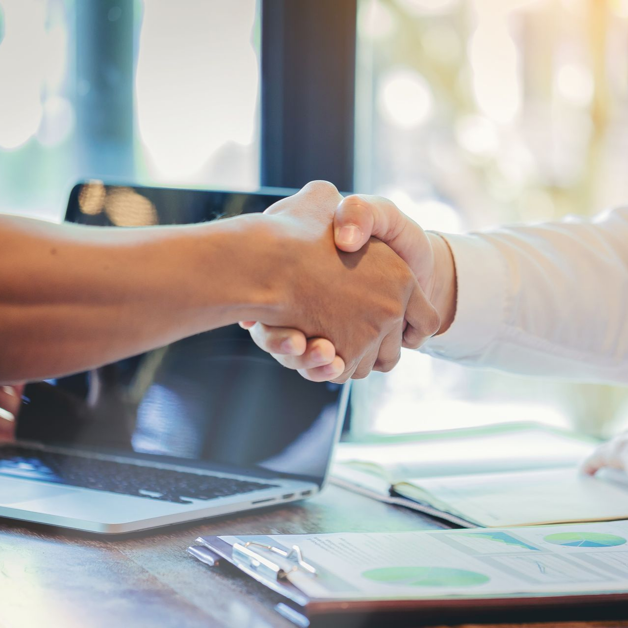 Deux personnes se serrent la main au-dessus d'un ordinateur portable et de documents posés sur un bureau.