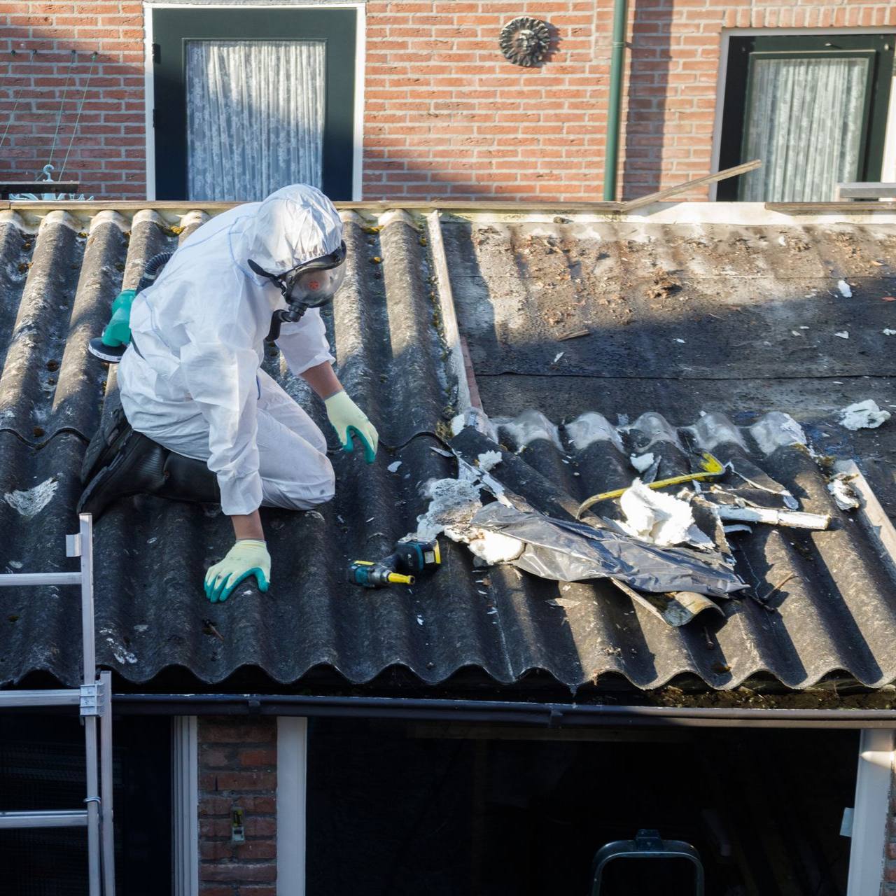 Une personne en combinaison de protection enlève des tuiles de toit en amiante.