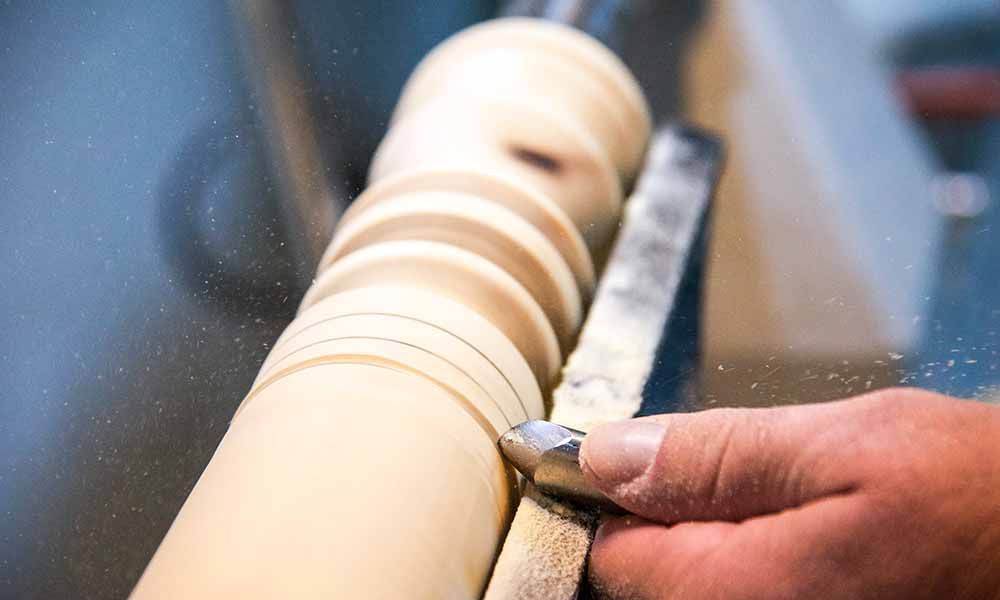 Eine Person schneidet ein Stück Holz mit einem Messer an einer Drechselmaschine.