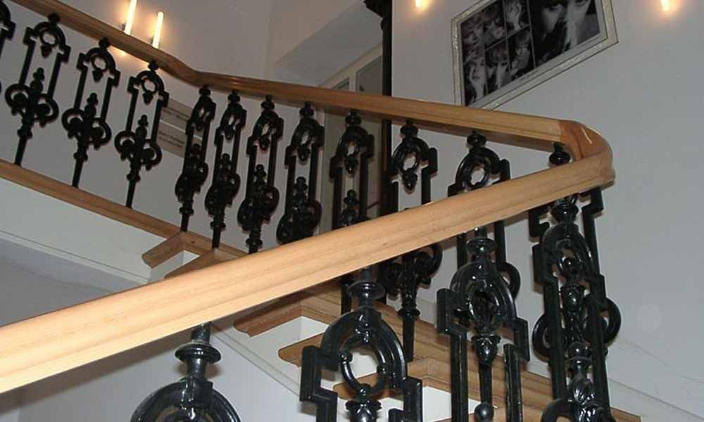 eine Treppe mit einem schwarzen Metallgeländer und einem Holzhandlauf