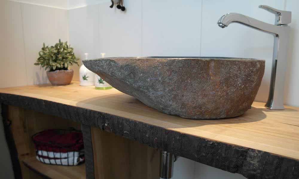 ein Steinwaschbecken sitzt auf einem Holztisch in einem Badezimmer .