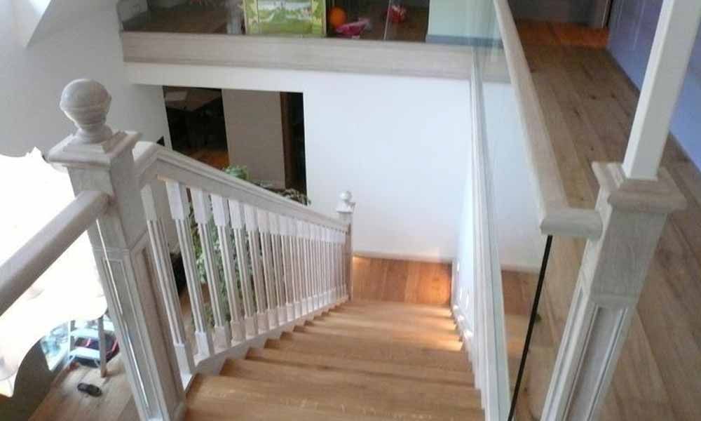 eine Holztreppe mit weißem Geländer und Glasgeländer führt zum zweiten Stock .