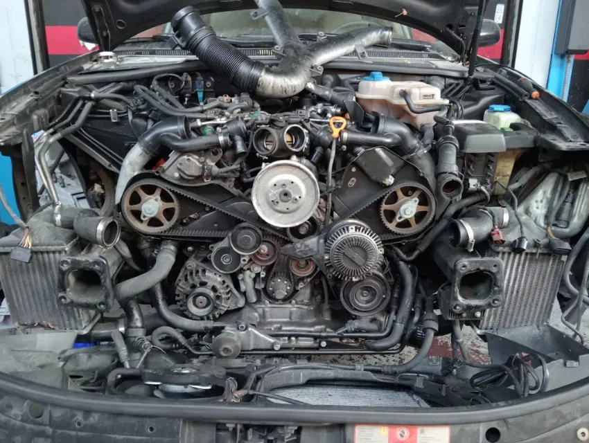 Parte delantera de un coche con el parachoques retirado, dejando al descubierto el motor, las correas, las poleas y los componentes del radiador.