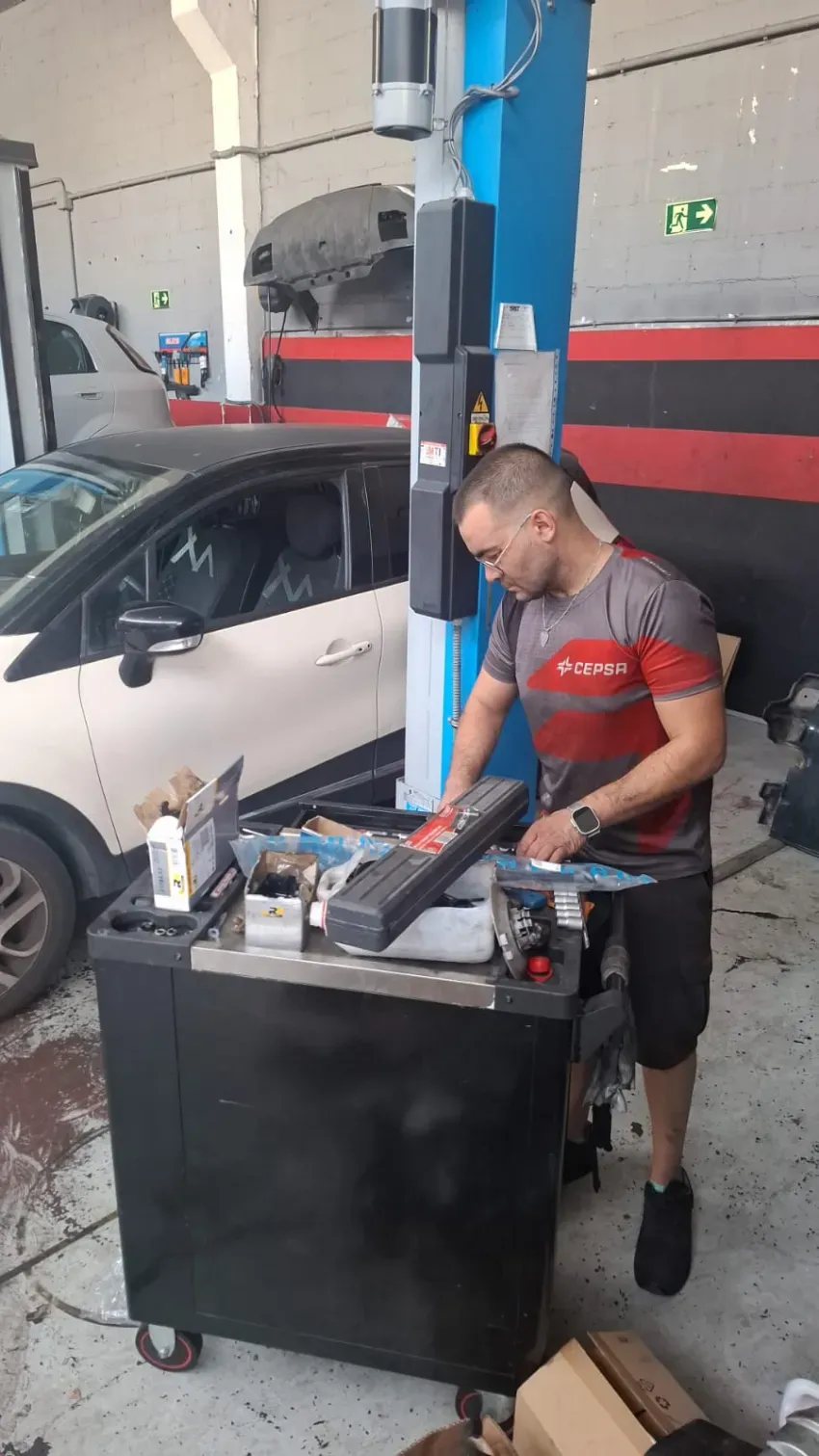 Mecánico trabajando en una máquina de equilibrado de neumáticos junto a un coche blanco en un garaje.