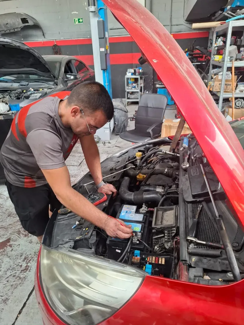 Mecánico trabajando bajo el capó de un coche rojo en un garaje.
