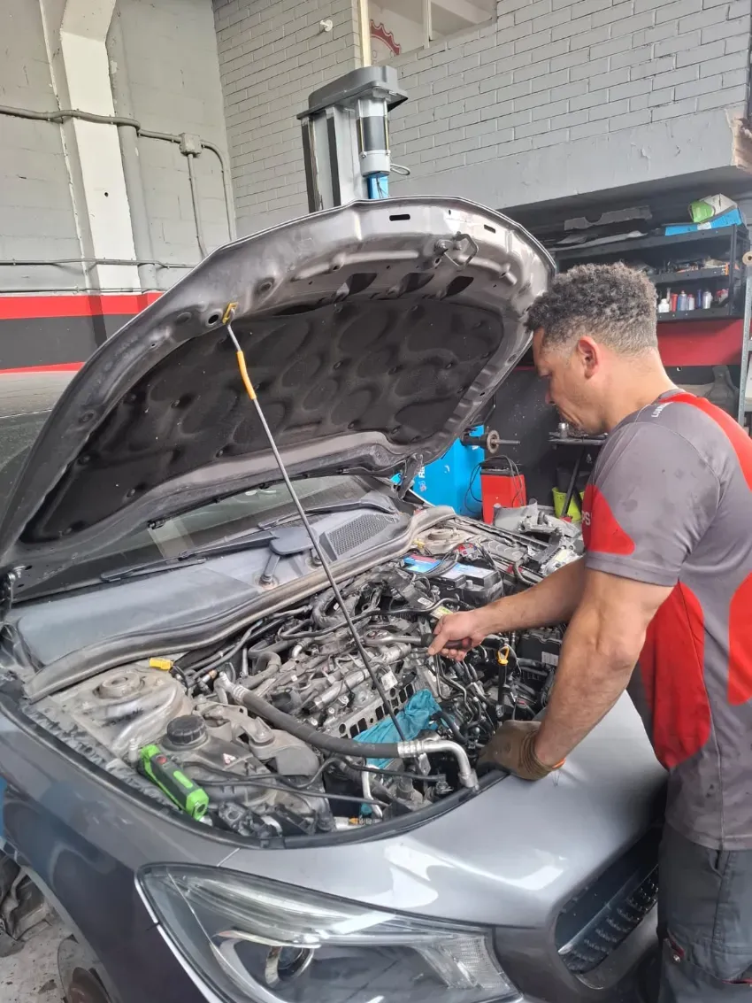 Mecánico inspeccionando el motor de un coche con el capó abierto en un garaje.