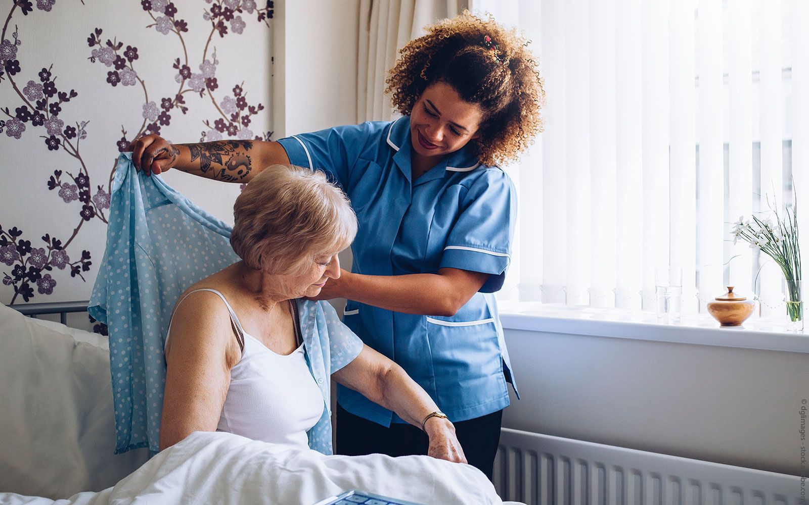 Eine Krankenschwester hilft einer älteren Frau beim Anziehen im Bett.