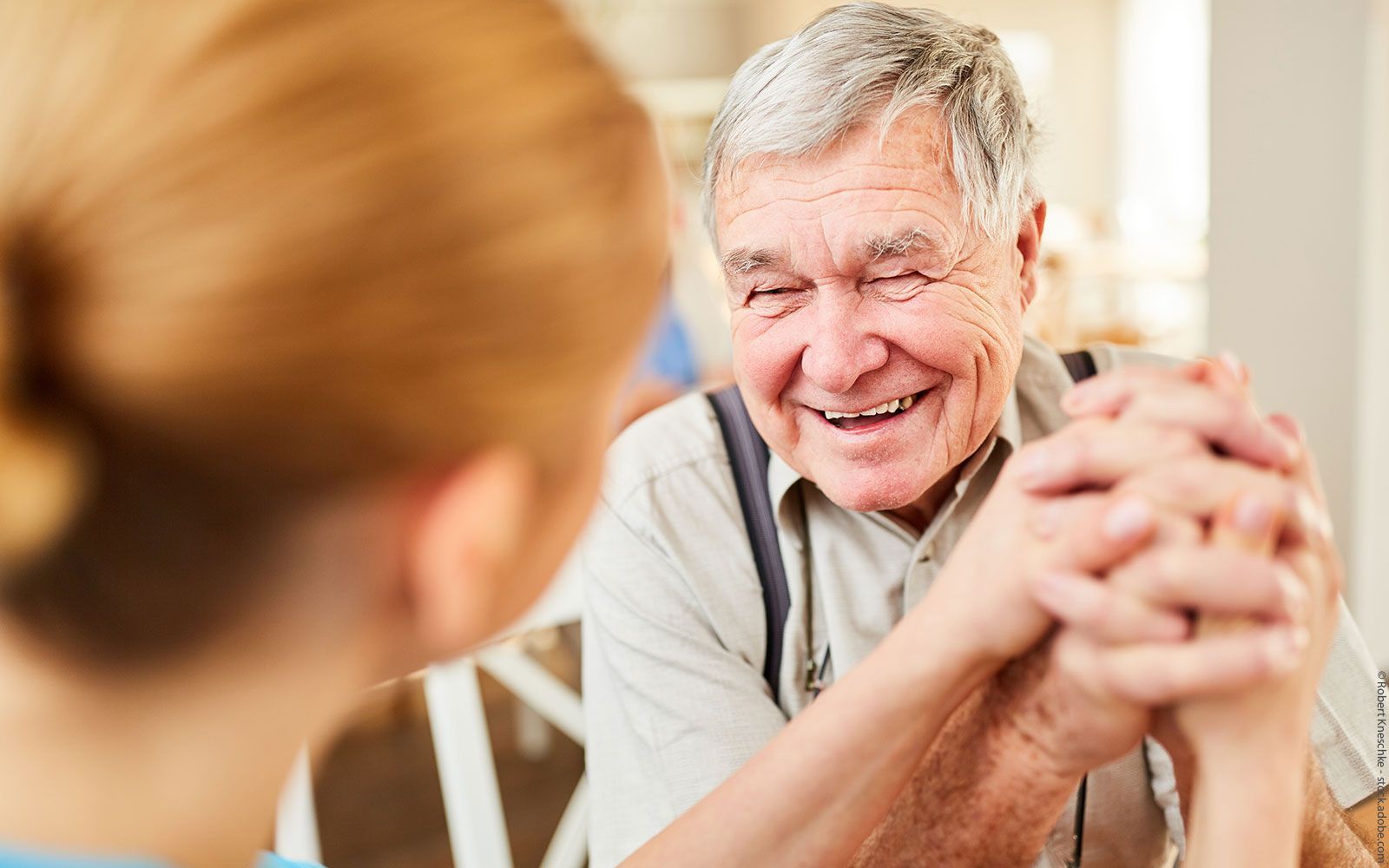 Ein älterer Mann hält eine Krankenschwester an der Hand und lächelt.