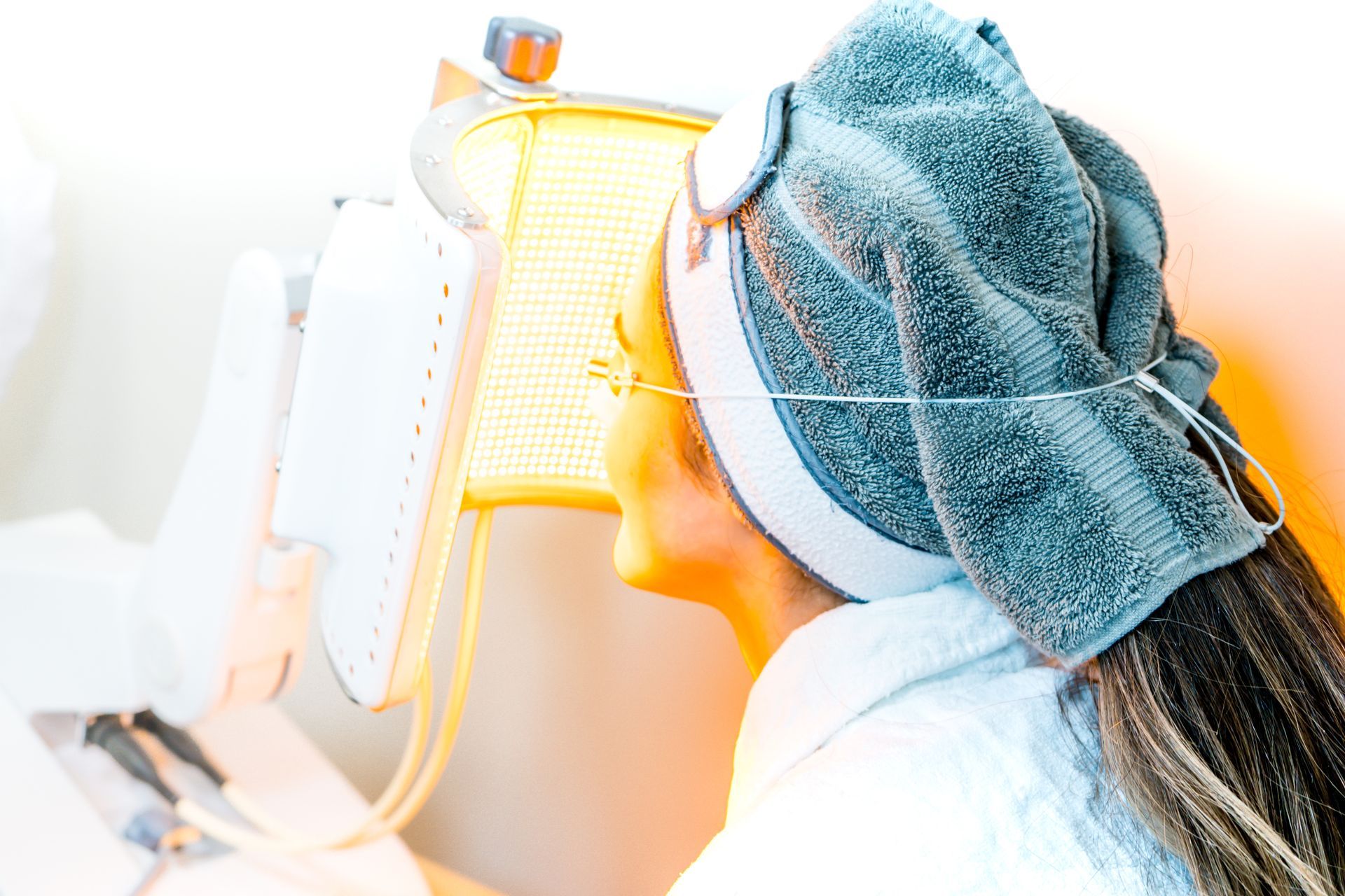 Frau mit Handtuch und LED-Lichttherapiegerät im Gesicht im Spa.