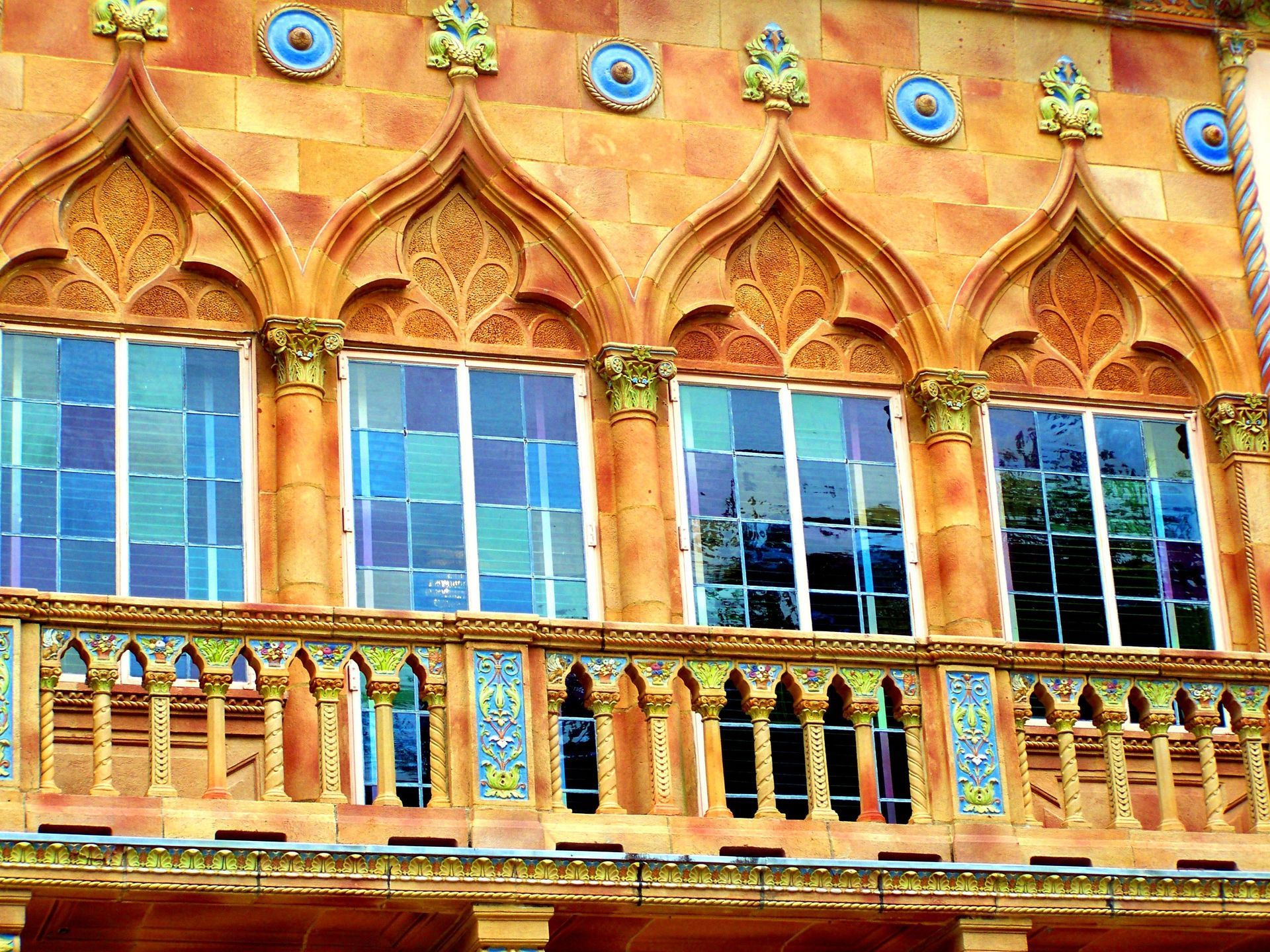 Verzierte Gebäudefassade mit Bogenfenstern, blauem Buntglas und dekorativen Balkonen.