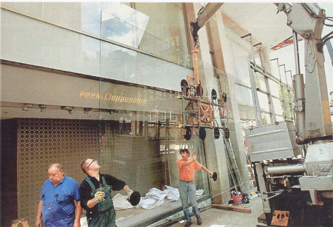 Arbeiter montieren mit einem Kran große Glasscheiben an einem Gebäude.