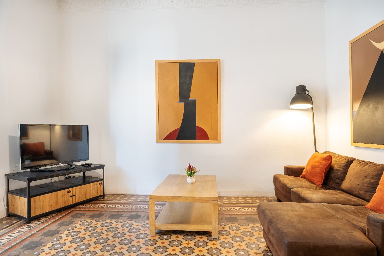Sala de estar moderna con sofá marrón, mueble para TV, mesa de centro, alfombra estampada, lámpara y arte abstracto en la pared.