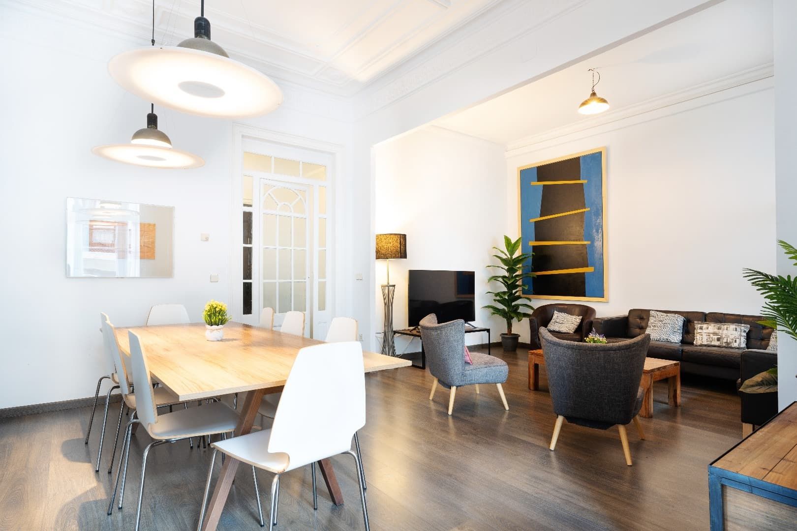 Luminoso y moderno salón-comedor diáfano con paredes blancas, suelos de madera y sillas azules y negras.