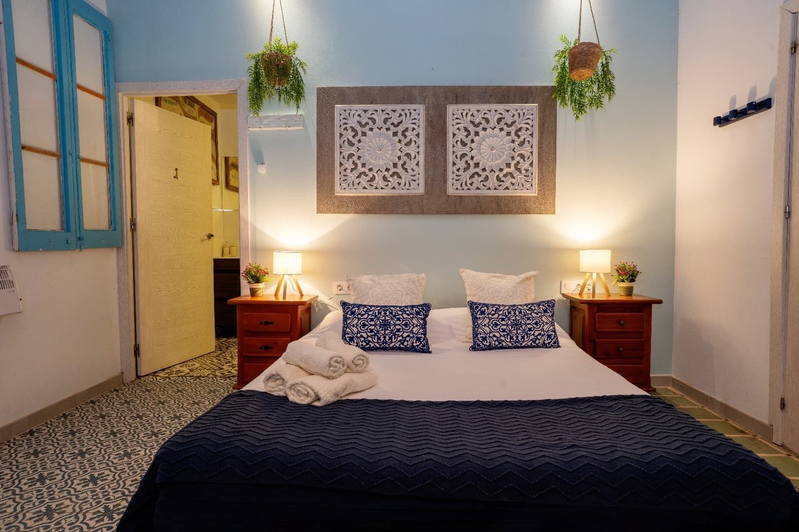 Habitación acogedora con cama, cuadros con motivos decorativos, lámparas de noche y plantas colgantes.