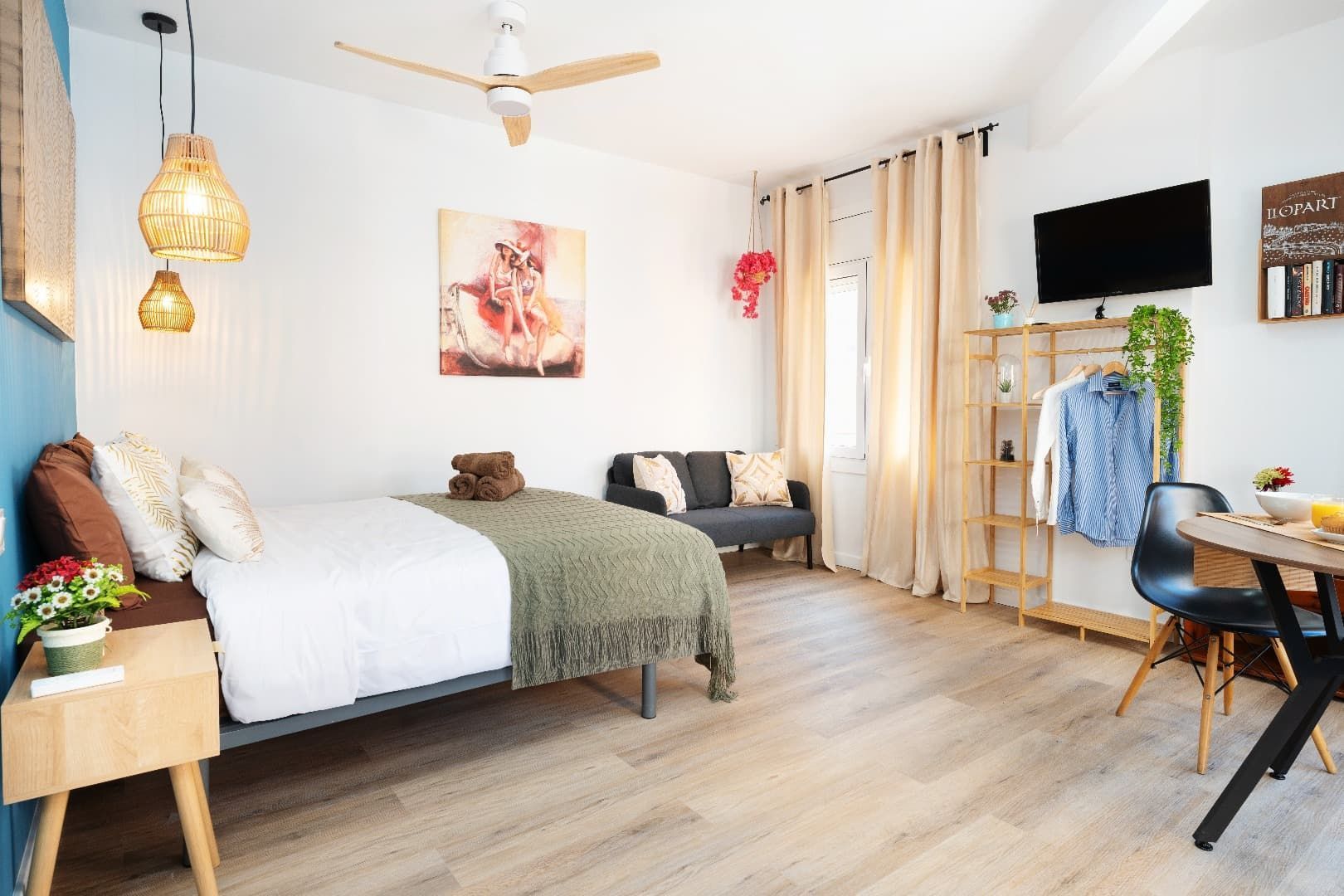 Habitación luminosa y moderna con cama, escritorio, televisor montado en la pared, cortinas y suelo de madera clara.