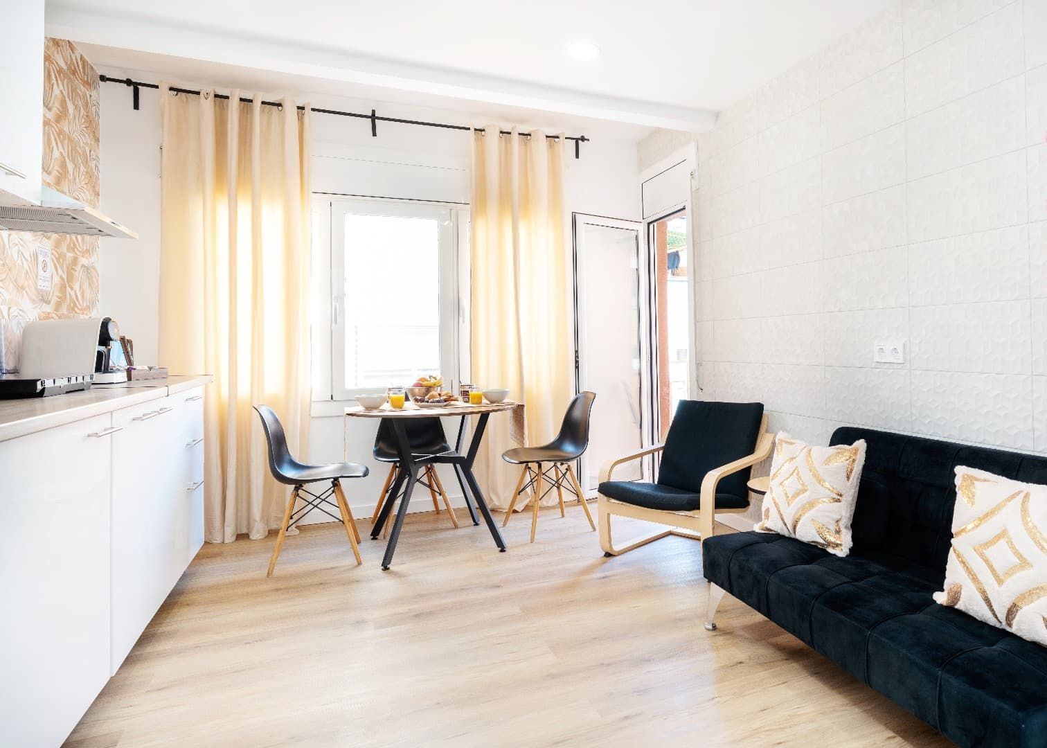 Comedor moderno y luminoso con sofá negro, cortinas amarillas y una mesita junto a una ventana soleada.