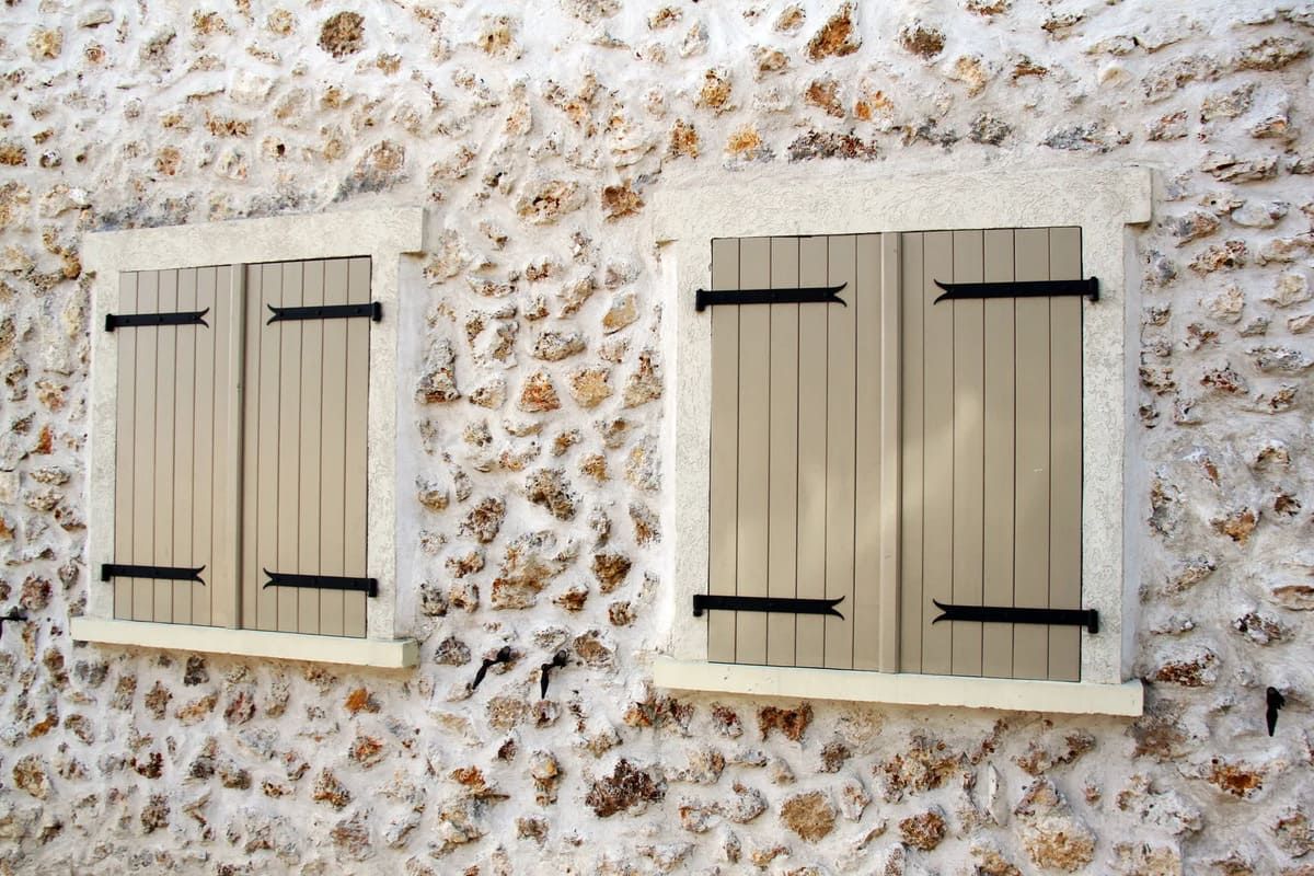 Deux volets battants beiges sur une façade en pierres