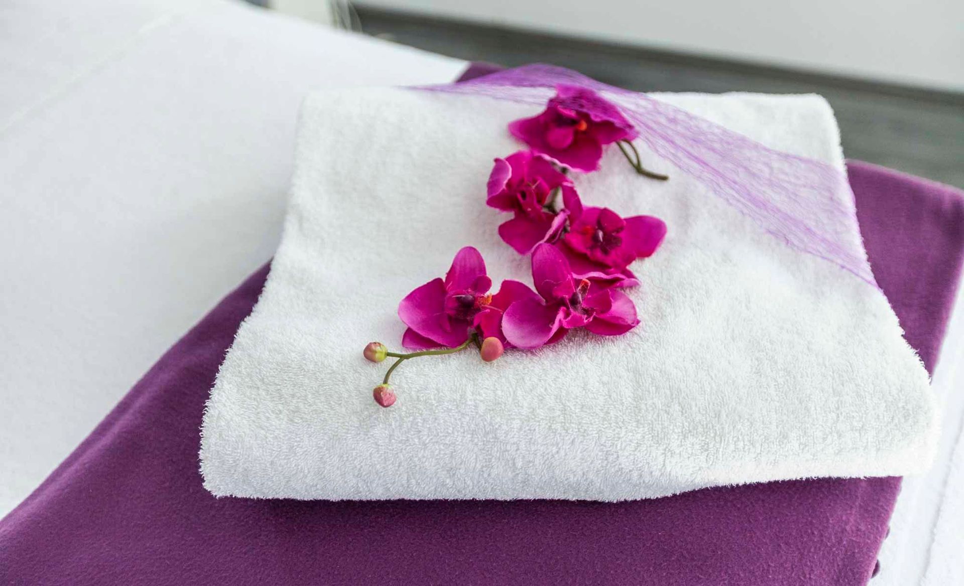 ein Stapel weißer Handtücher in der Beauty & Wellness Lounge mit pinken Orchideenblüten darauf .
