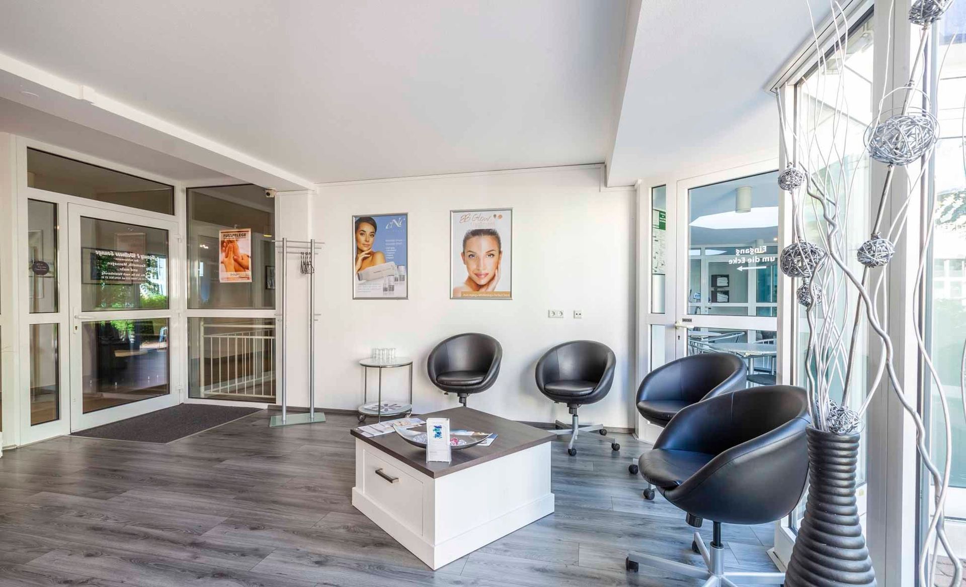 Wartebereich in der Beauty & Wellness Lounge mit Stühlen , einem Tisch und einem Bild an der Wand .