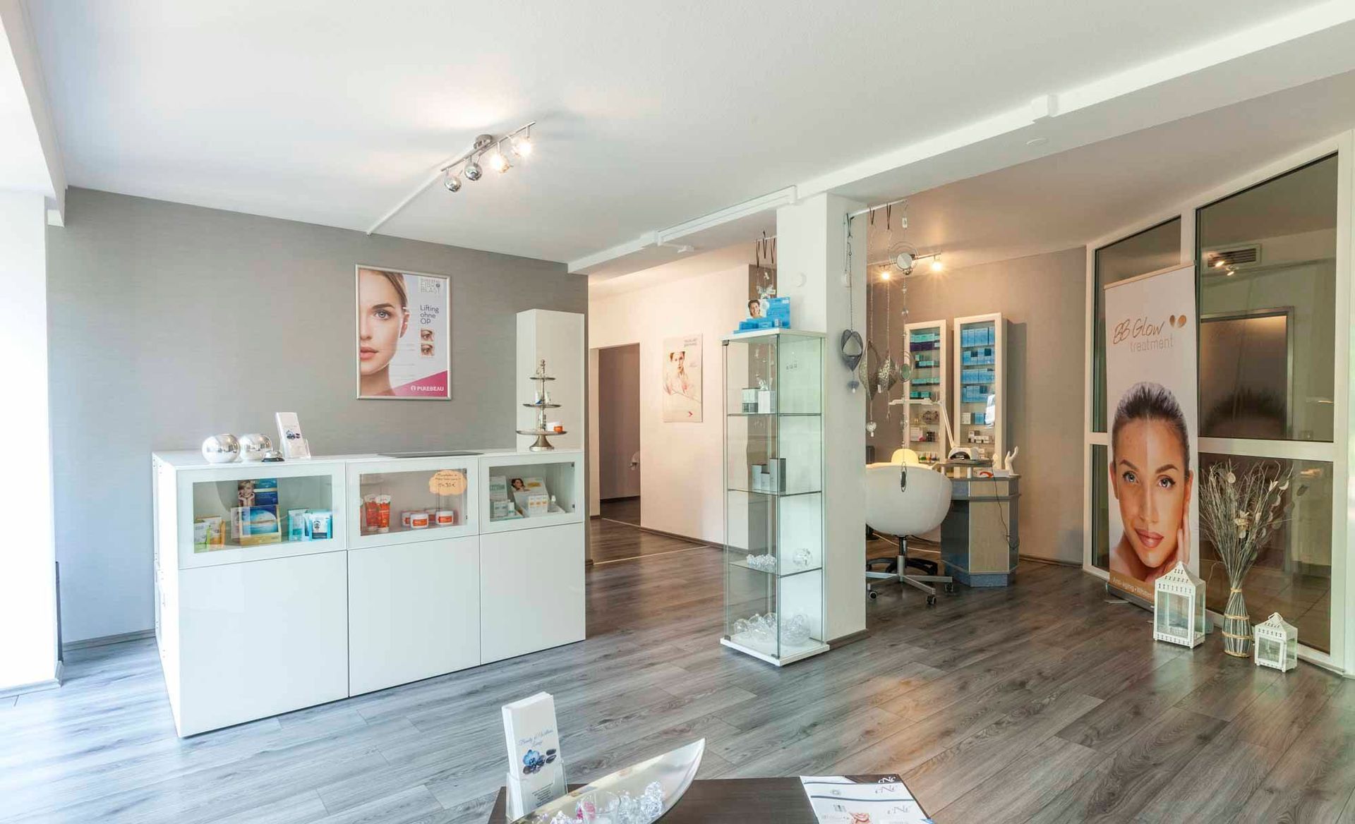 Eingangsbereich in der Beauty & Wellness Lounge mit Holzboden , weißen Möbeln und einem Spiegel .